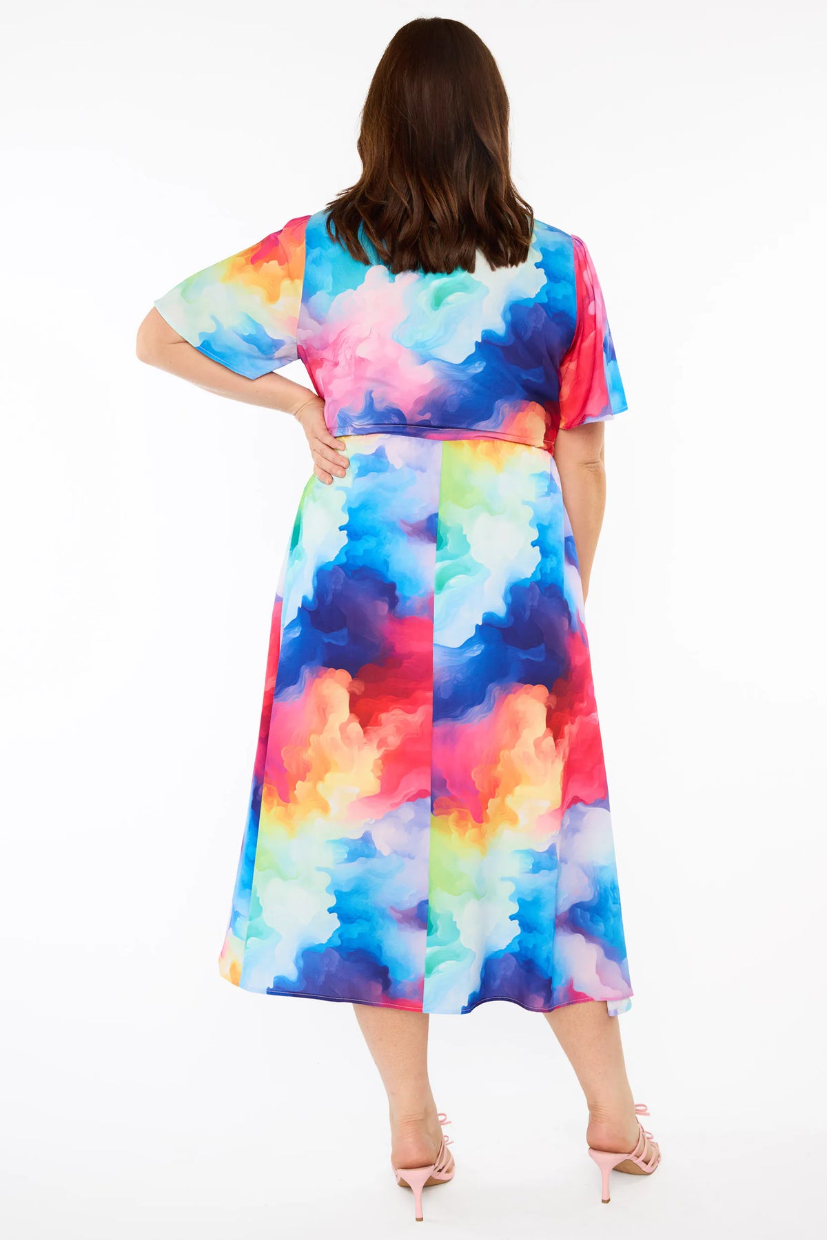 A woman modelling a short-sleeve midi dress with a vibrant watercolour tie-dye pattern in shades of blue, pink, yellow, green, and purple, set against a plain white studio background.
