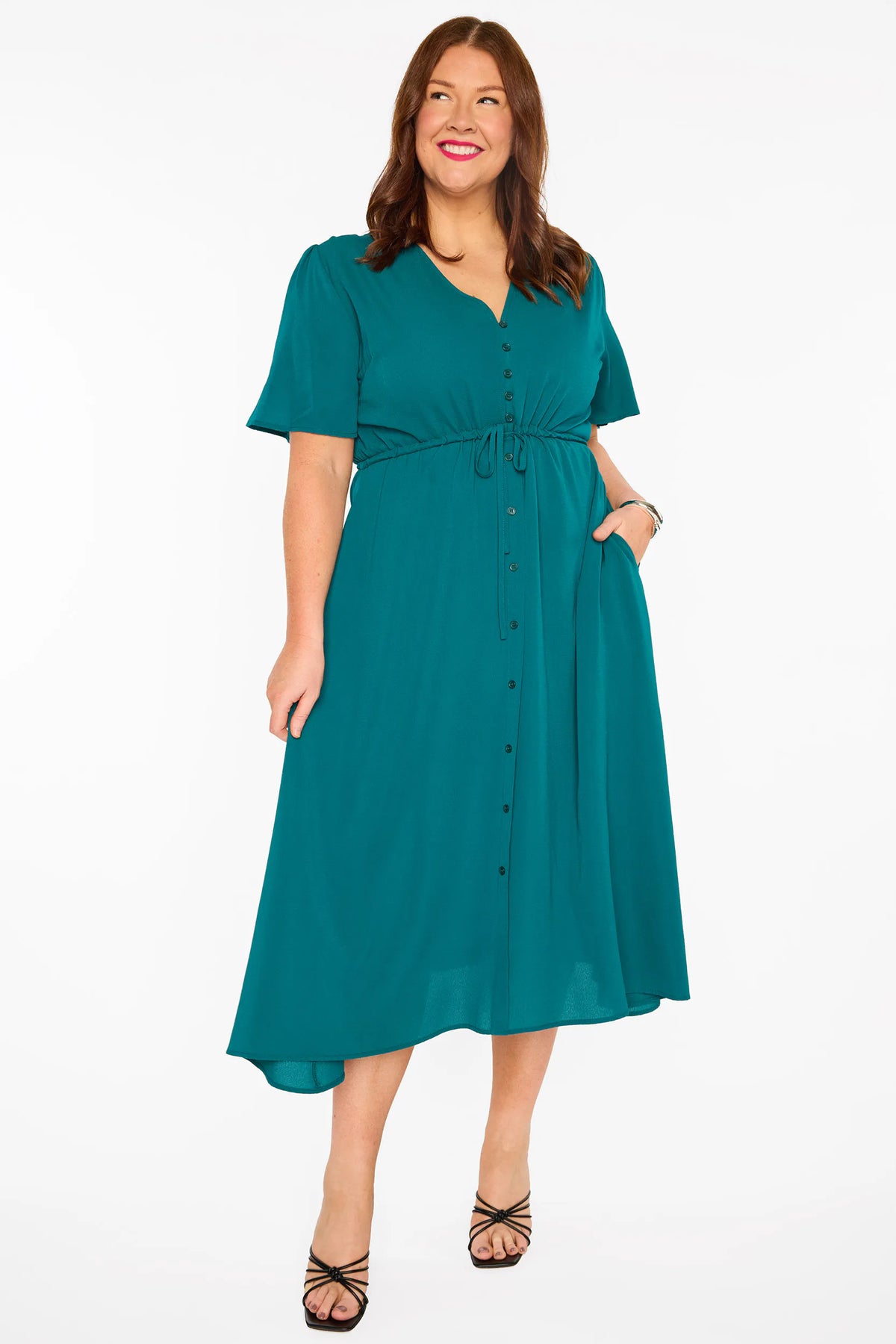 A woman modelling a teal green midi dress with short sleeves, a button-down front, and a tie waist, set against a plain white studio background.