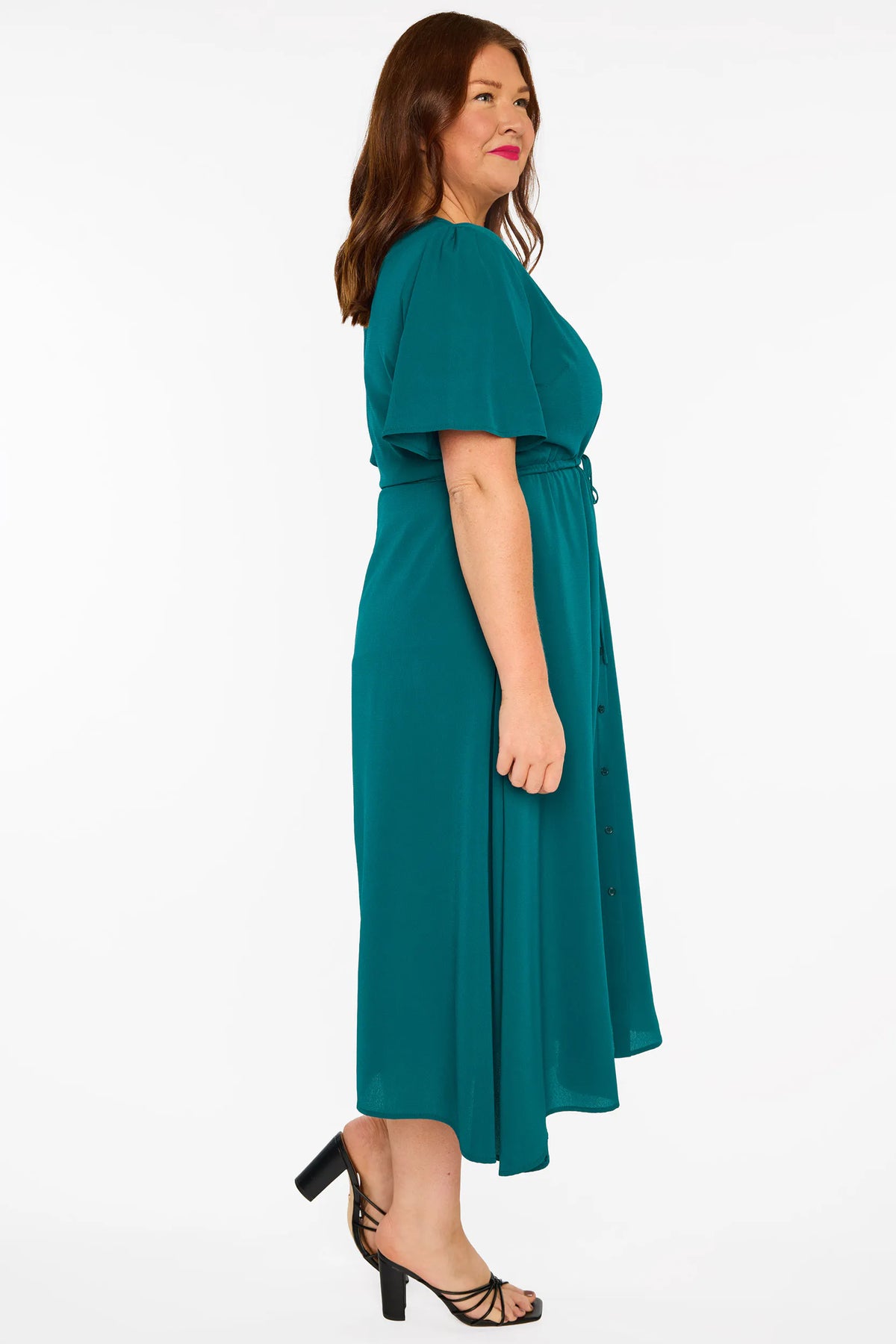A woman modelling a teal green midi dress with short sleeves, a button-down front, and a tie waist, set against a plain white studio background.