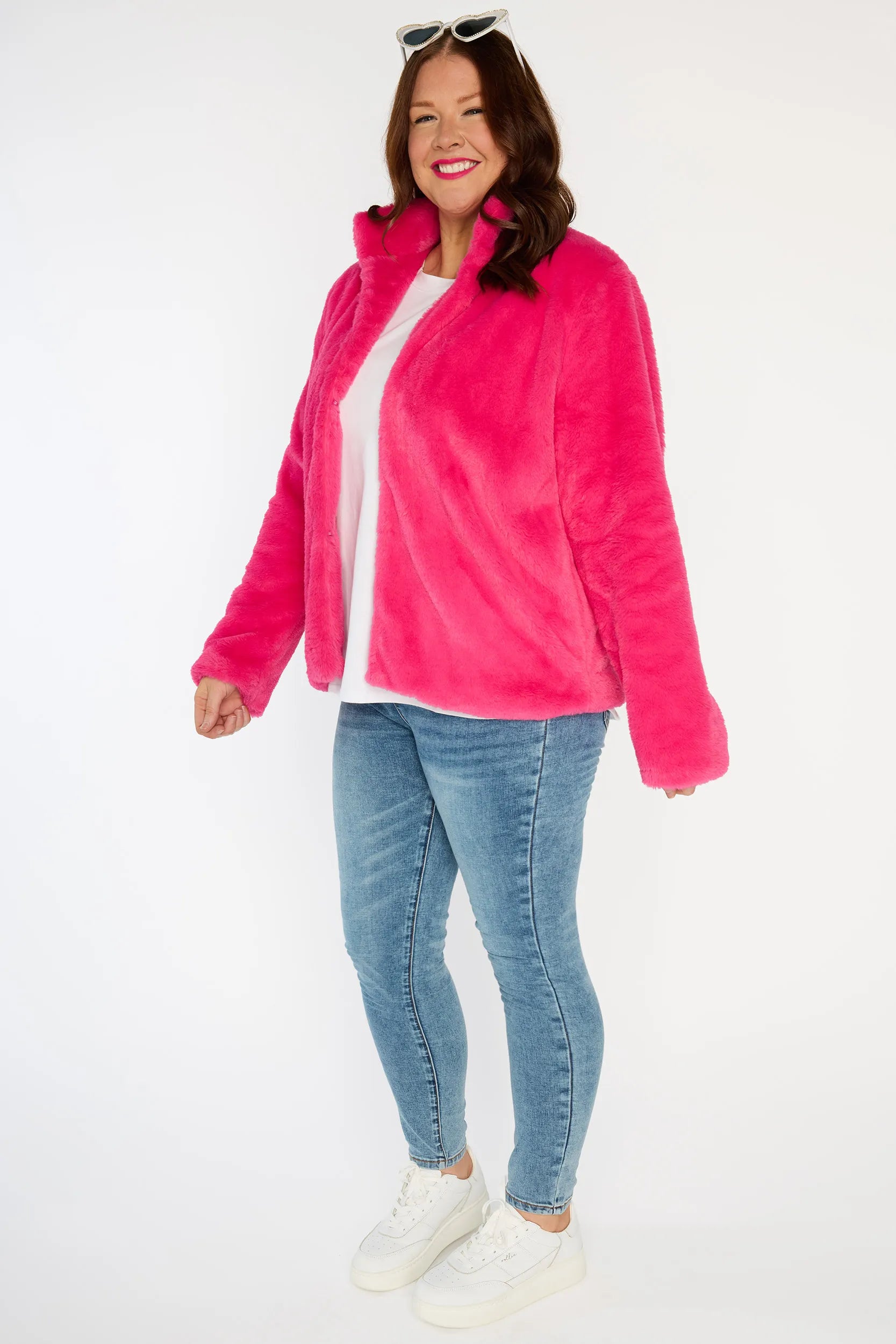 Person wearing a bright pink fleece jacket, white shirt, blue jeans, and white sneakers on a white background
