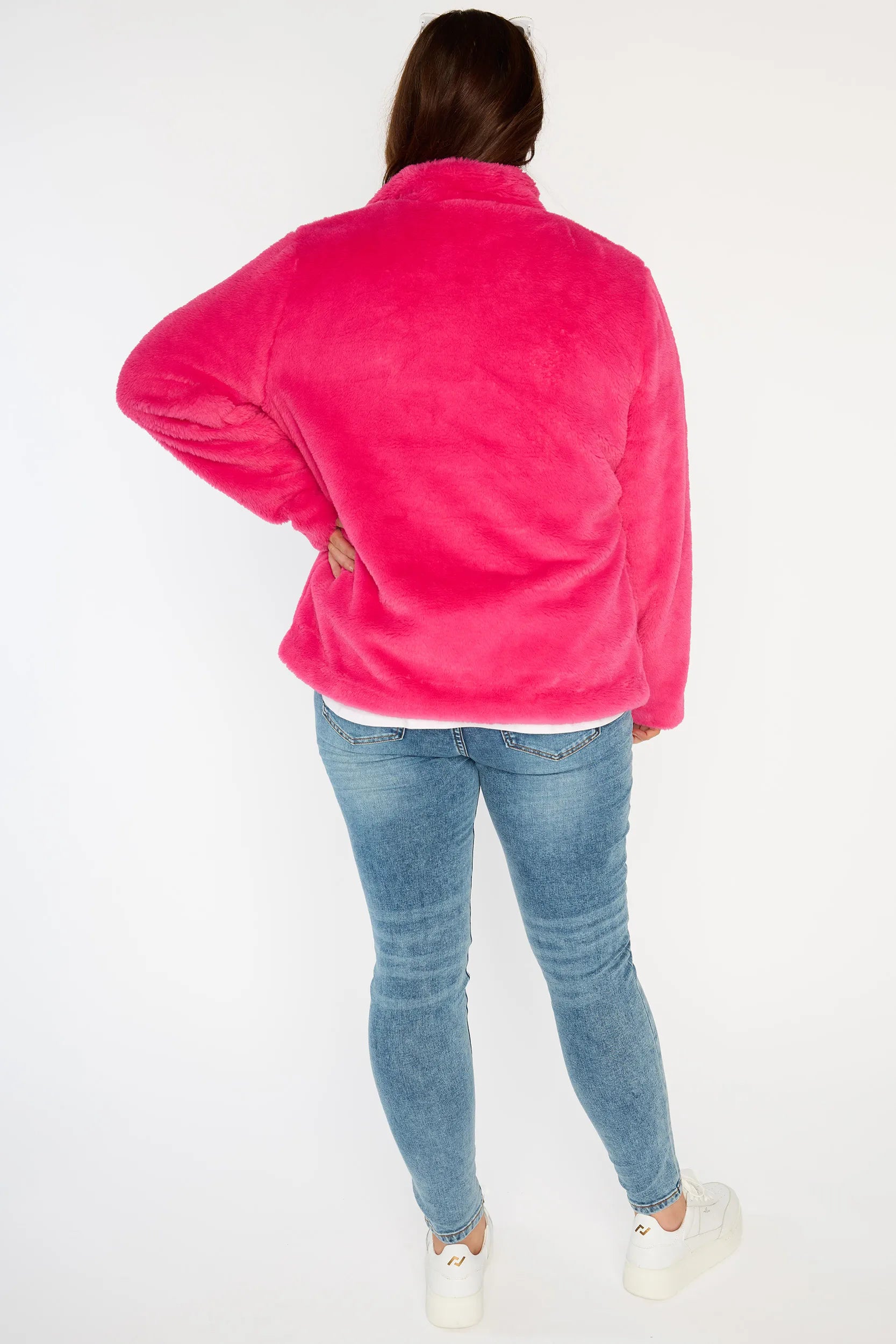 Person wearing a bright pink fleece jacket, white shirt, blue jeans, and white sneakers on a white background