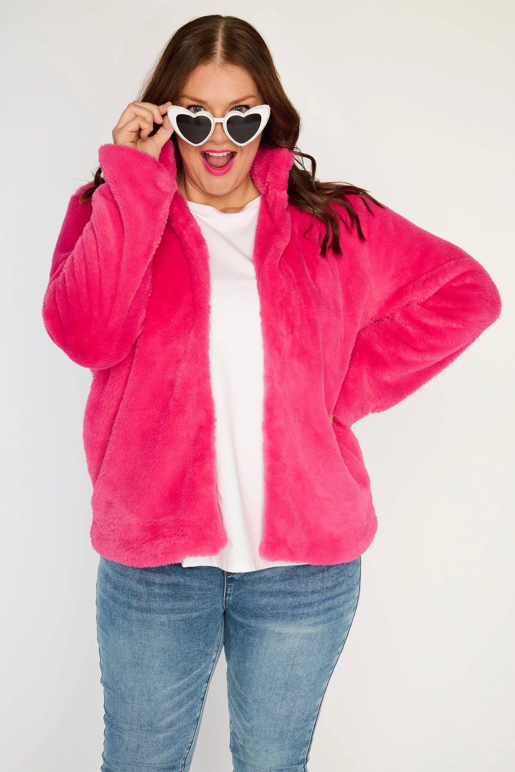 Person wearing a bright pink fleece jacket, white shirt, blue jeans, and white sneakers on a white background