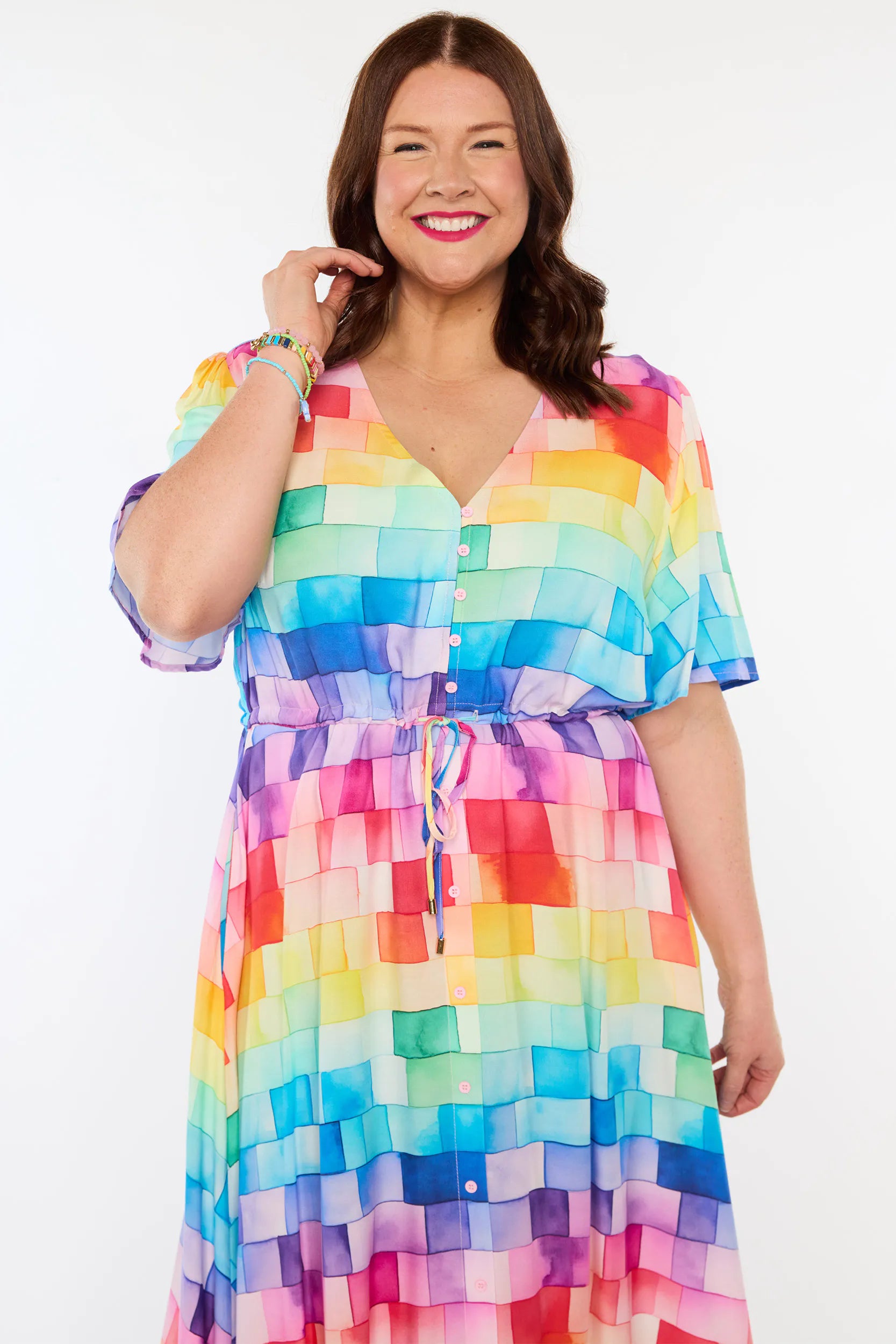 A woman modelling a short-sleeve midi dress with a rainbow tile print, featuring a V-neckline and side pockets.