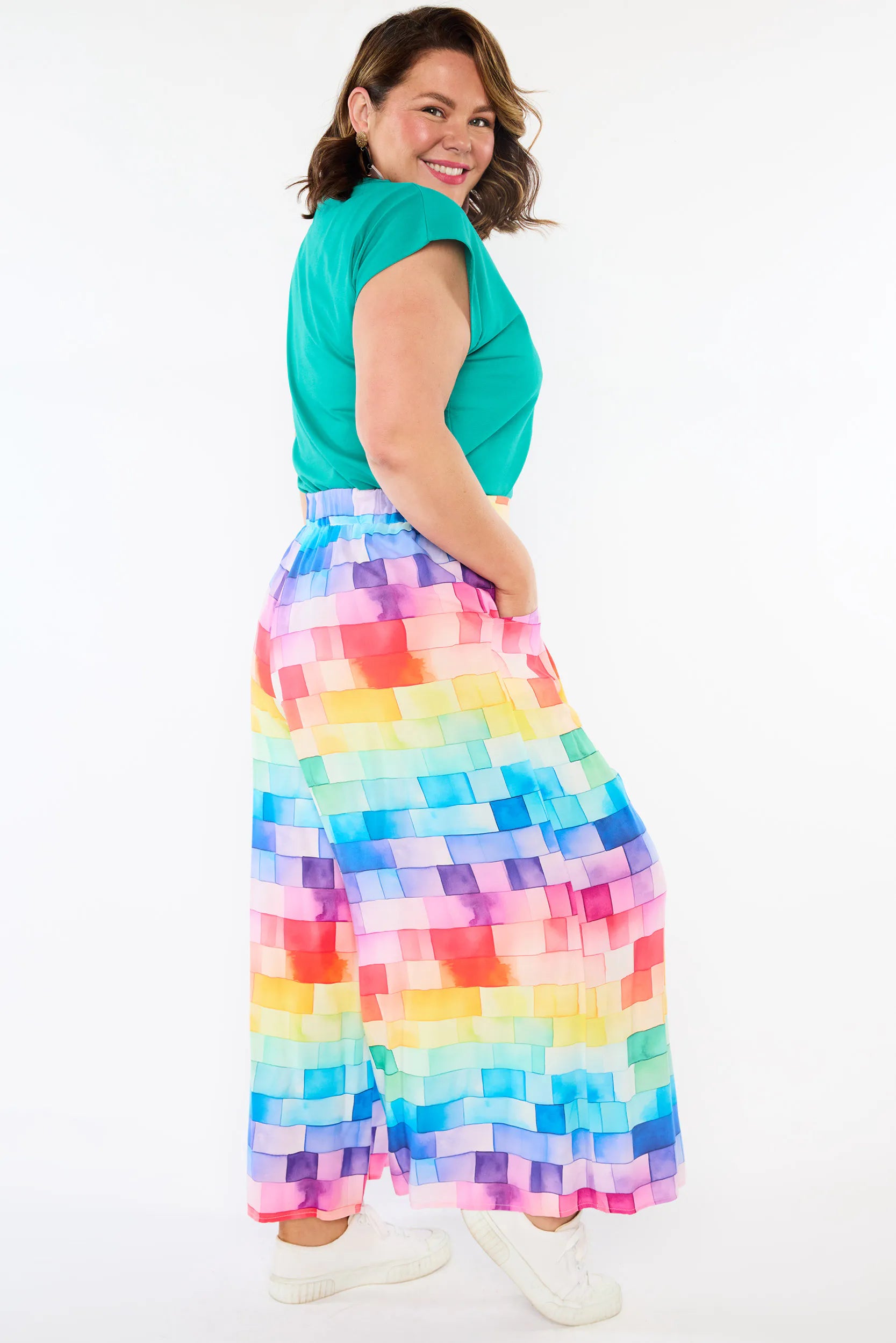 A woman wearing a bright green short-sleeve top and a colorful rainbow pixelated maxi skirt, posing against a plain white background.