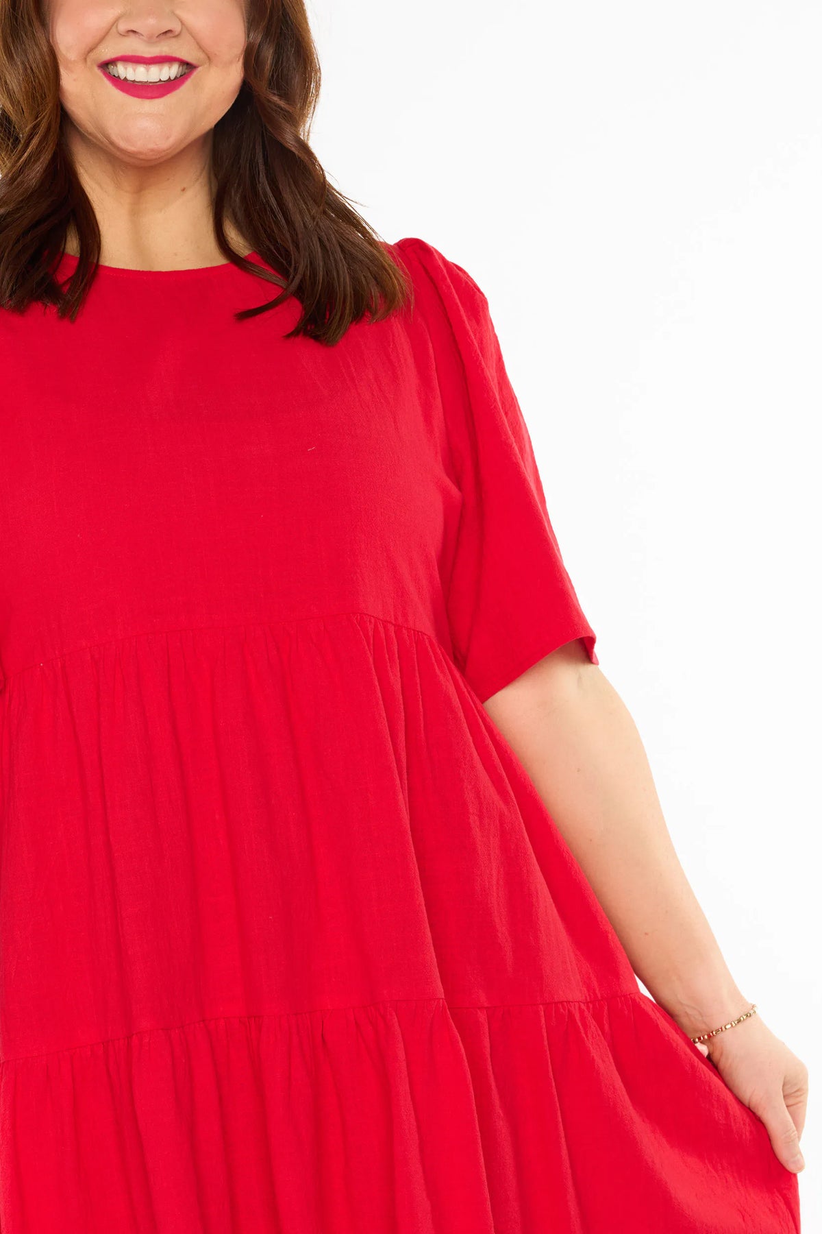 A close-up of a woman modelling a bright red tiered mini dress with short puff sleeves, against a plain white studio background.