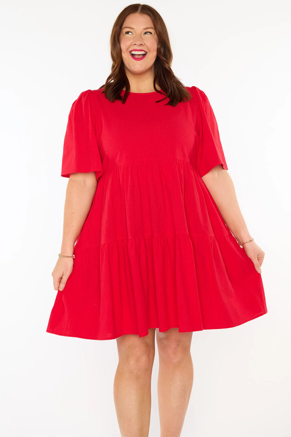 A woman modelling a bright red short-sleeve tiered dress against a plain white studio background.