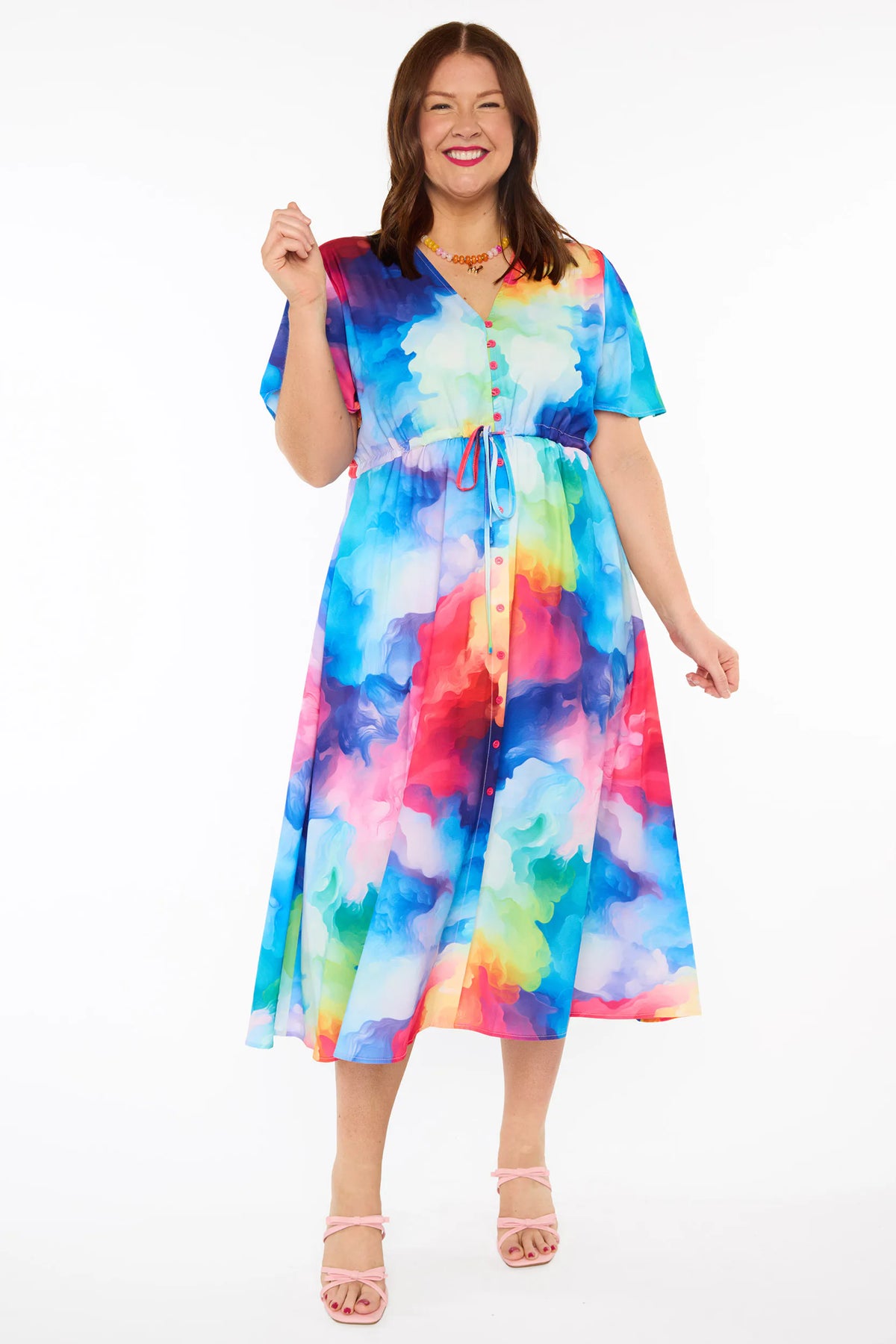 A woman modelling a short-sleeve midi dress with a vibrant watercolour tie-dye pattern in shades of blue, pink, yellow, green, and purple, set against a plain white studio background.