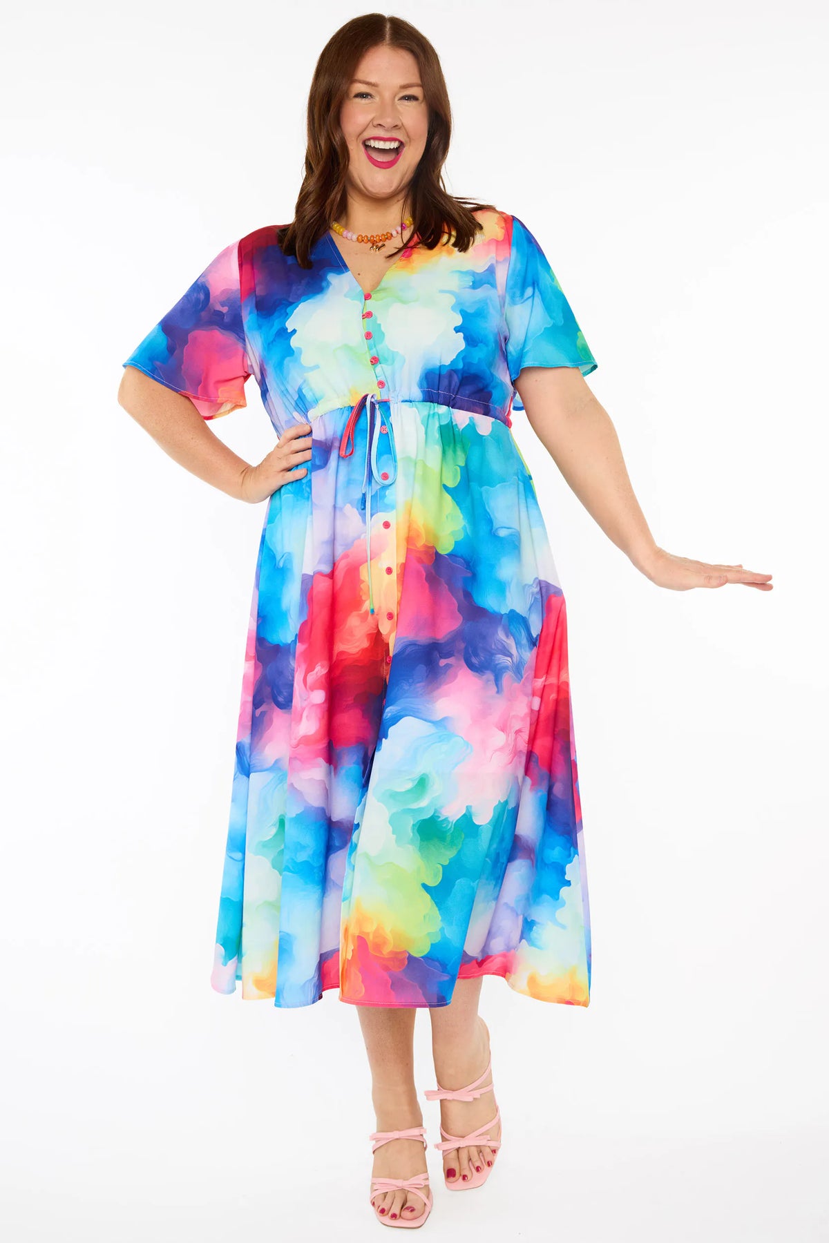 A woman modelling a short-sleeve midi dress with a vibrant watercolour tie-dye pattern in shades of blue, pink, yellow, green, and purple, set against a plain white studio background.