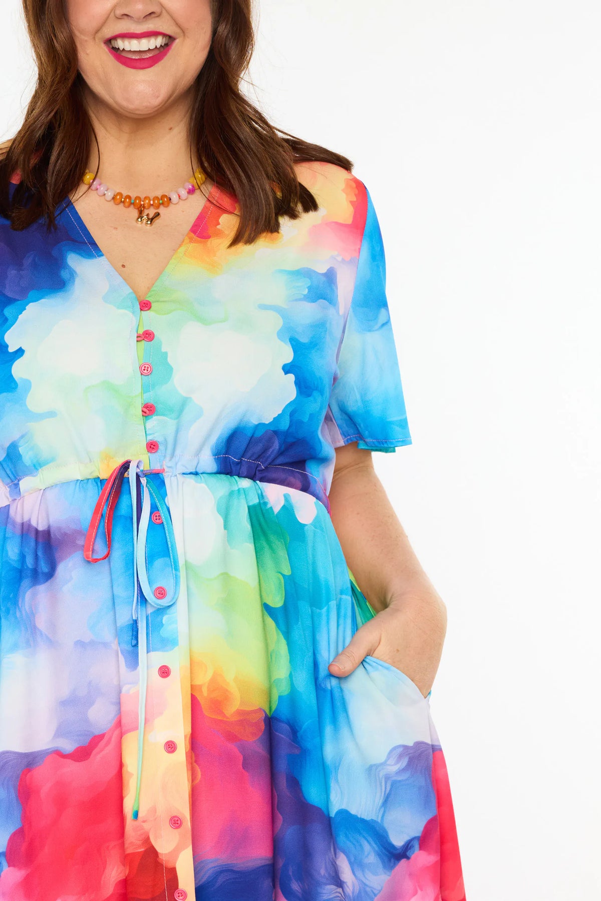 Close up of a woman modelling a short-sleeve midi dress with a vibrant watercolour tie-dye pattern in shades of blue, pink, yellow, green, and purple, set against a plain white studio background.