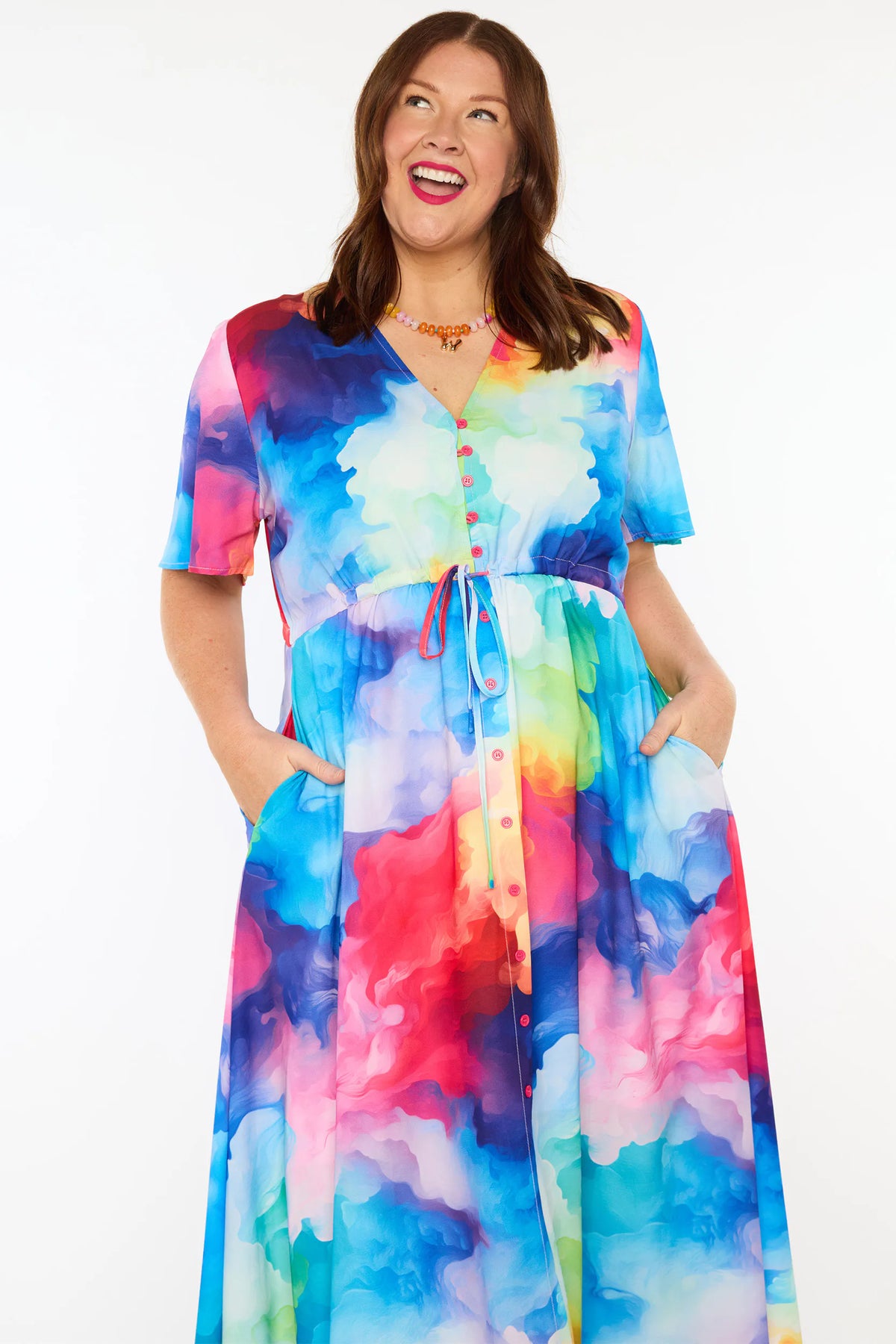 A woman modelling a short-sleeve midi dress with a vibrant watercolour tie-dye pattern in shades of blue, pink, yellow, green, and purple, set against a plain white studio background.