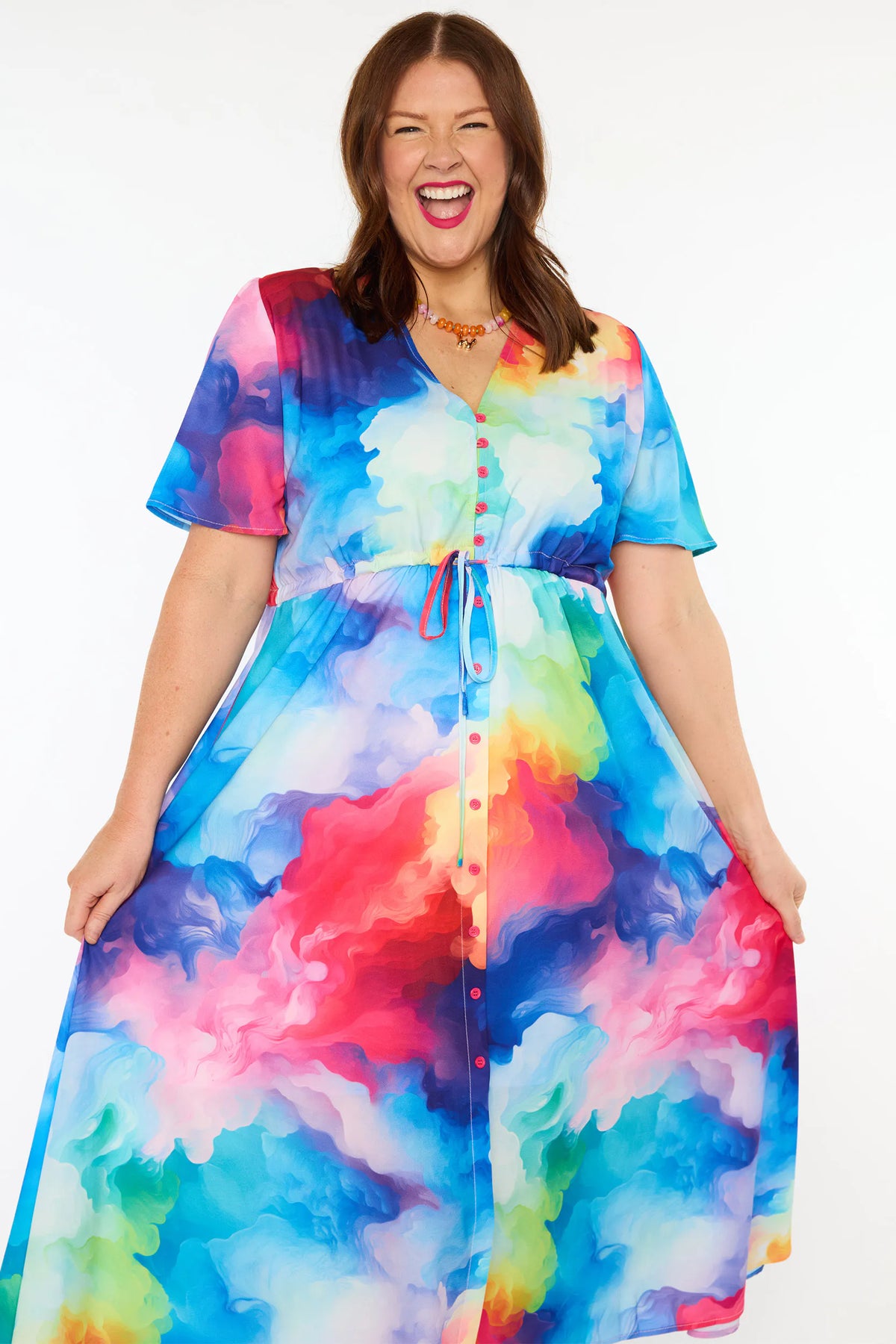 A woman modelling a short-sleeve midi dress with a vibrant watercolour tie-dye pattern in shades of blue, pink, yellow, green, and purple, set against a plain white studio background.