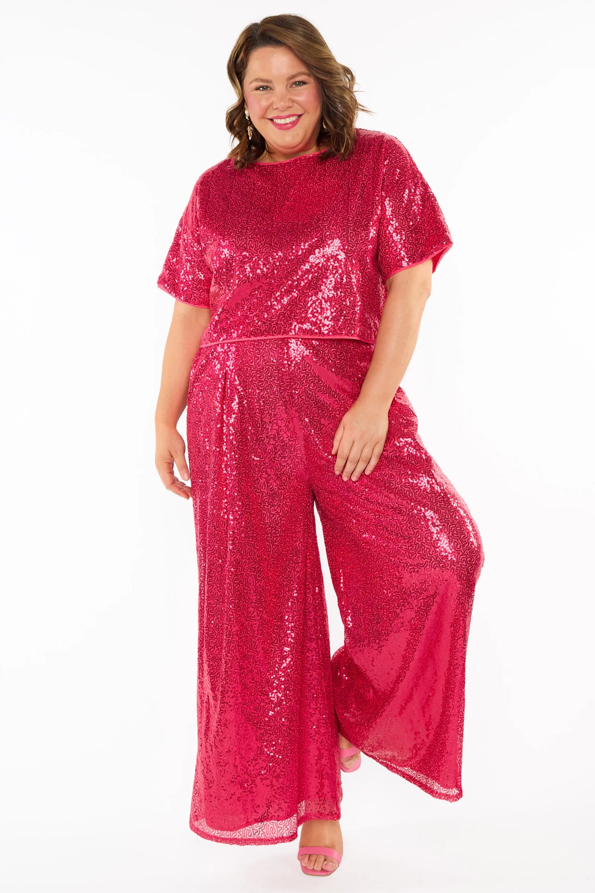 A woman modelling a bright pink sequins short sleeves top and wide leg pant, standing against a plain white studio background.