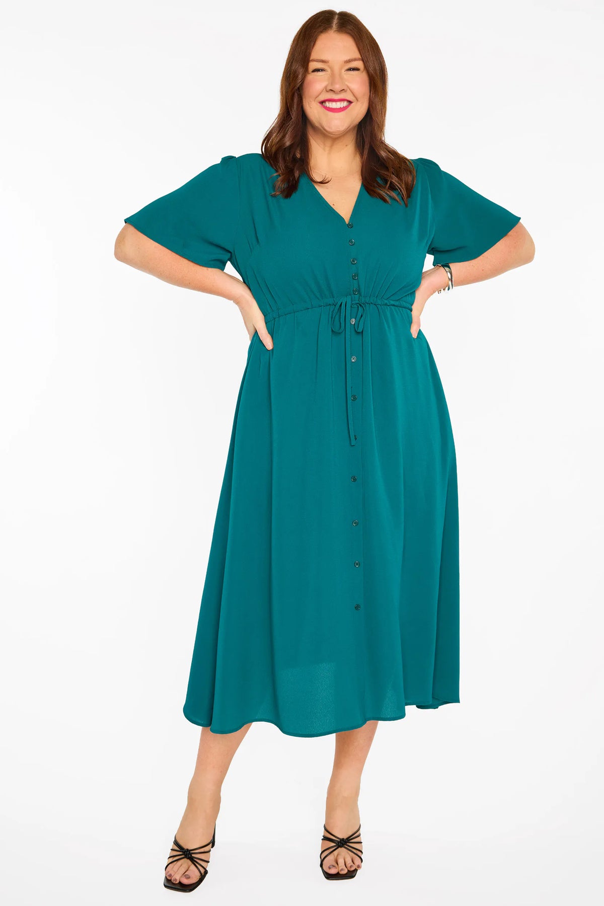 A woman modelling a teal green midi dress with short sleeves, a button-down front, and a tie waist, set against a plain white studio background.