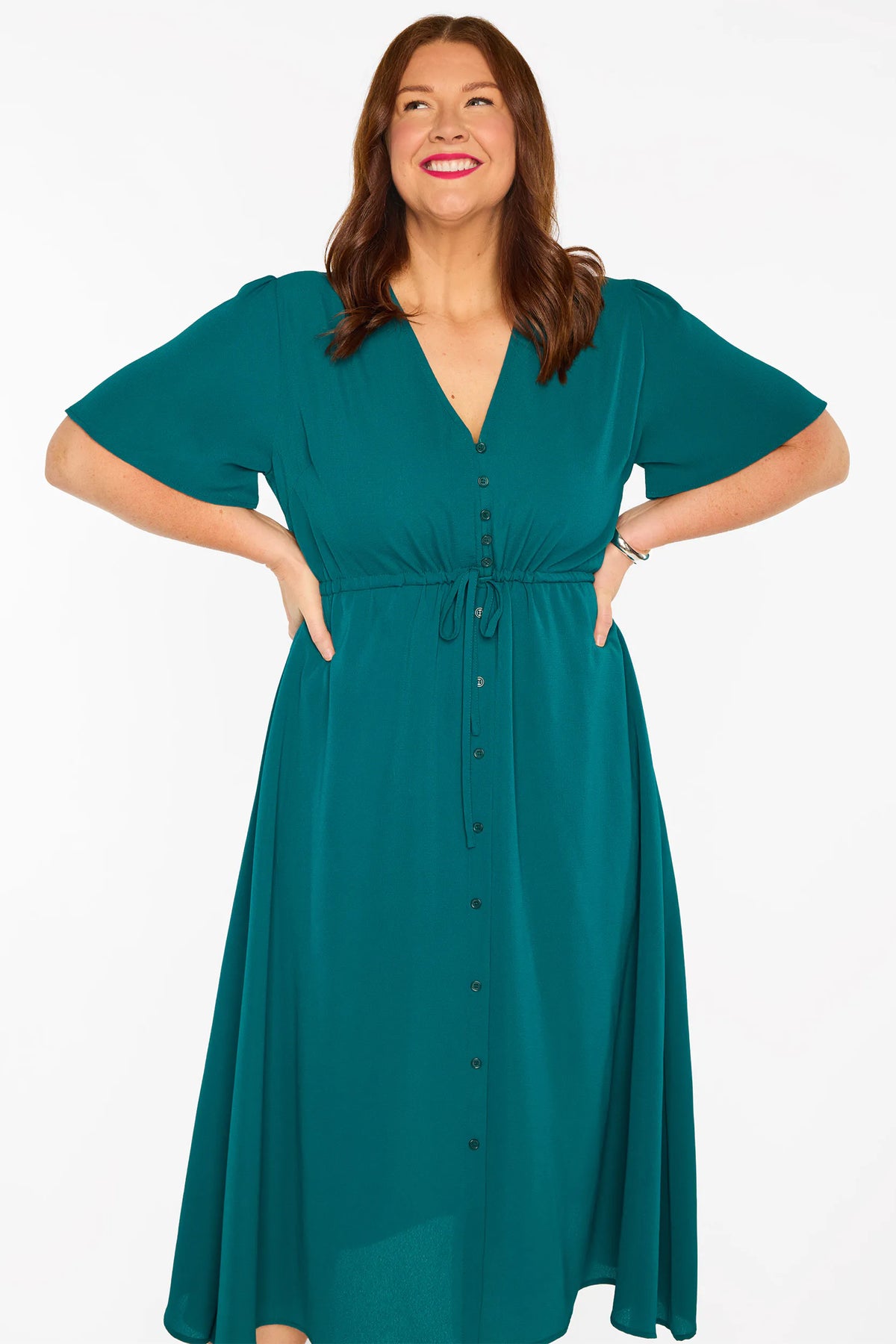A woman modelling a teal green midi dress with short sleeves, a button-down front, and a tie waist, set against a plain white studio background.