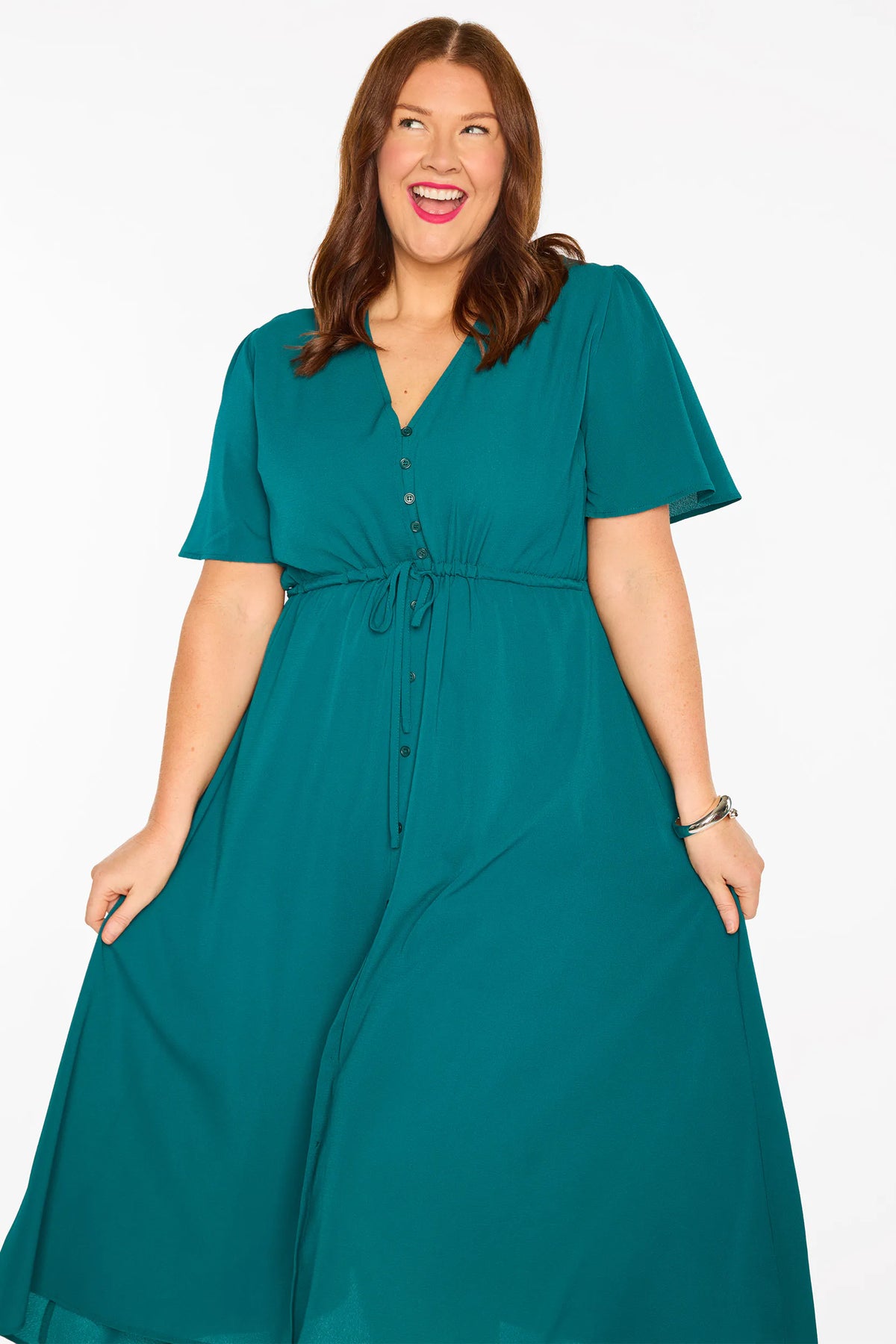 A woman modelling a teal green midi dress with short sleeves, a button-down front, and a tie waist, set against a plain white studio background.