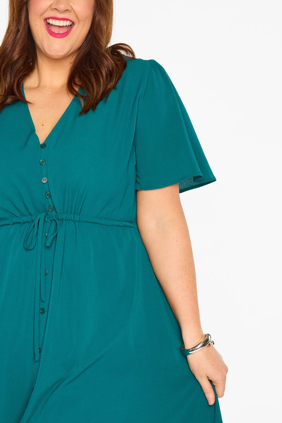 A woman modelling a teal green midi dress with short sleeves, a button-down front, and a tie waist, set against a plain white studio background.