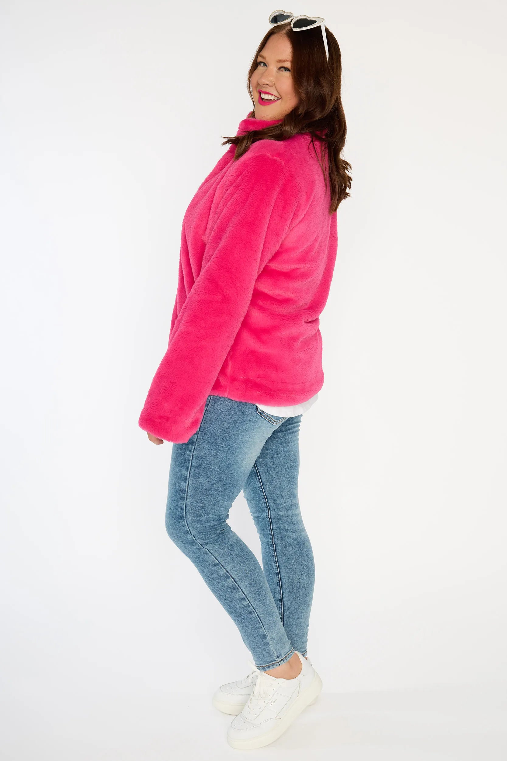 Person wearing a bright pink fleece jacket, white shirt, blue jeans, and white sneakers on a white background