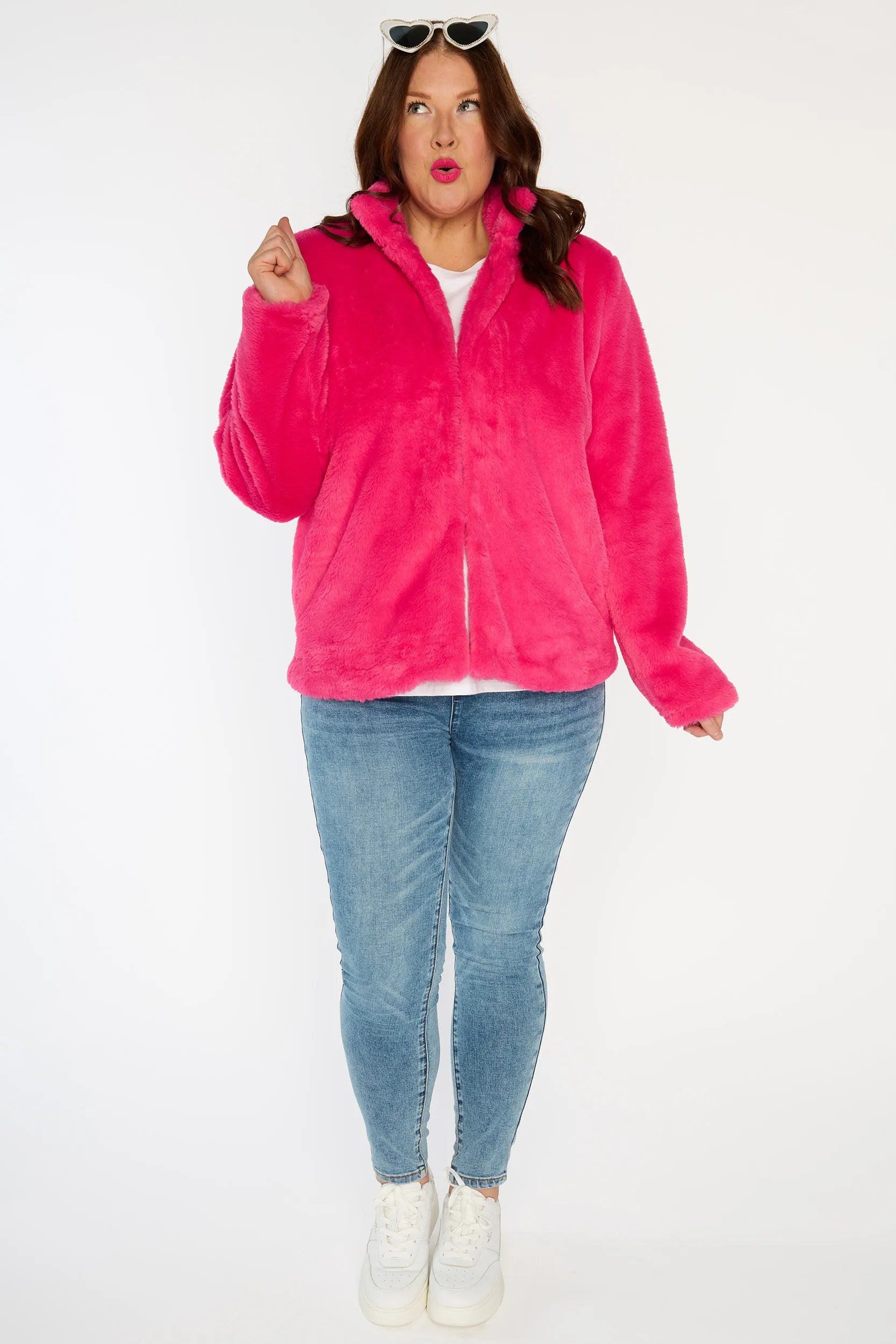Person wearing a bright pink fleece jacket, white shirt, blue jeans, and white sneakers on a white background