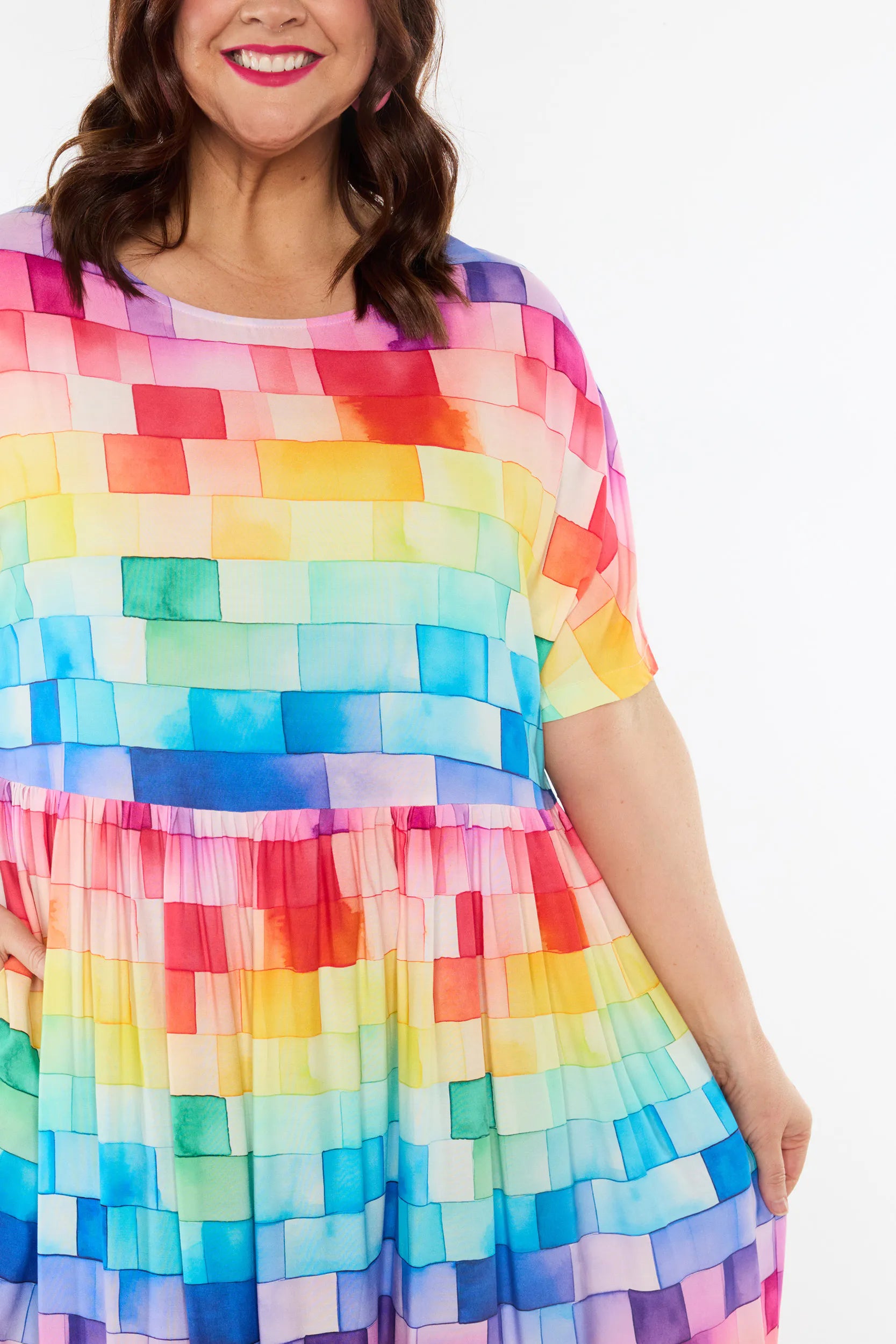 A woman wearing a short-sleeve tiered dress with a colourful rainbow block pattern, shown against a plain white background.