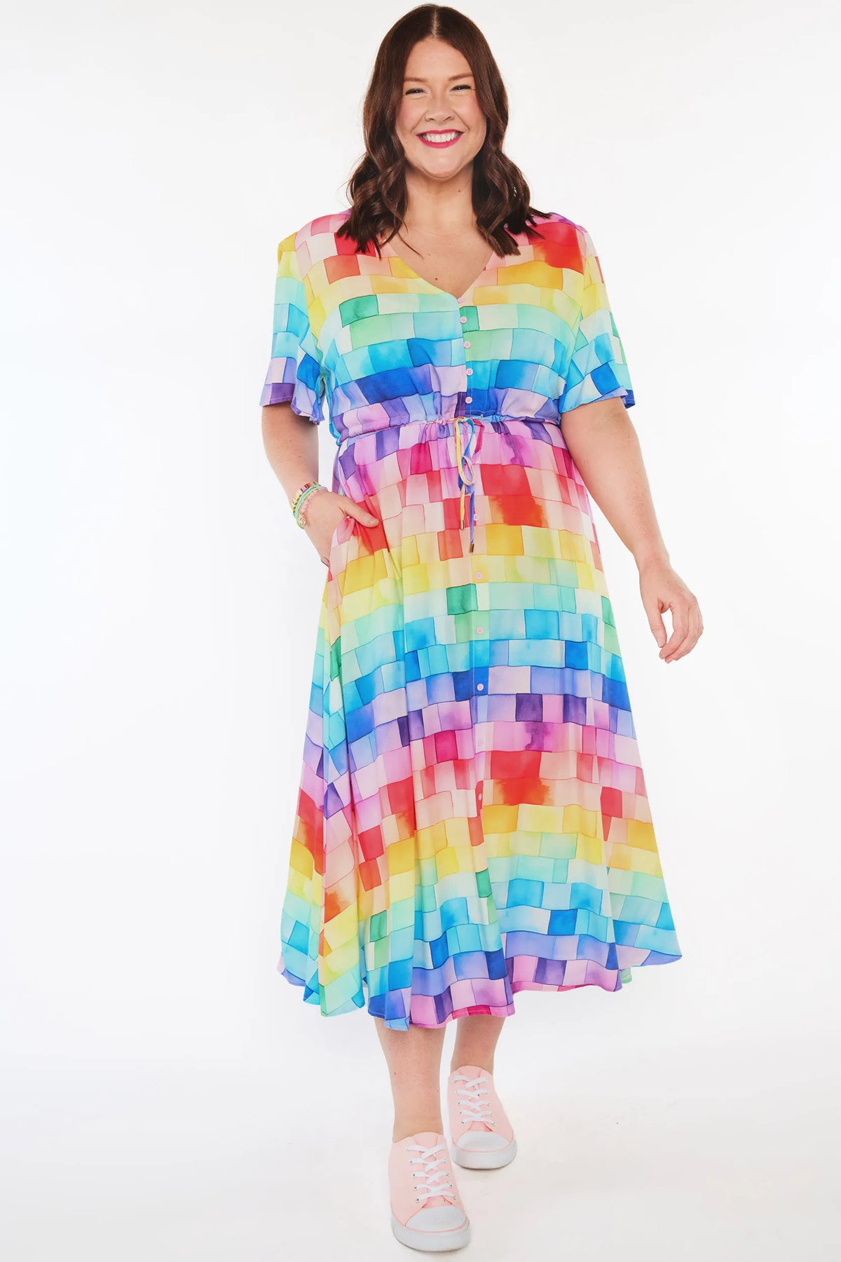 A woman modeling a short-sleeve midi dress with a colorful rainbow block pattern, standing against a plain white studio background.