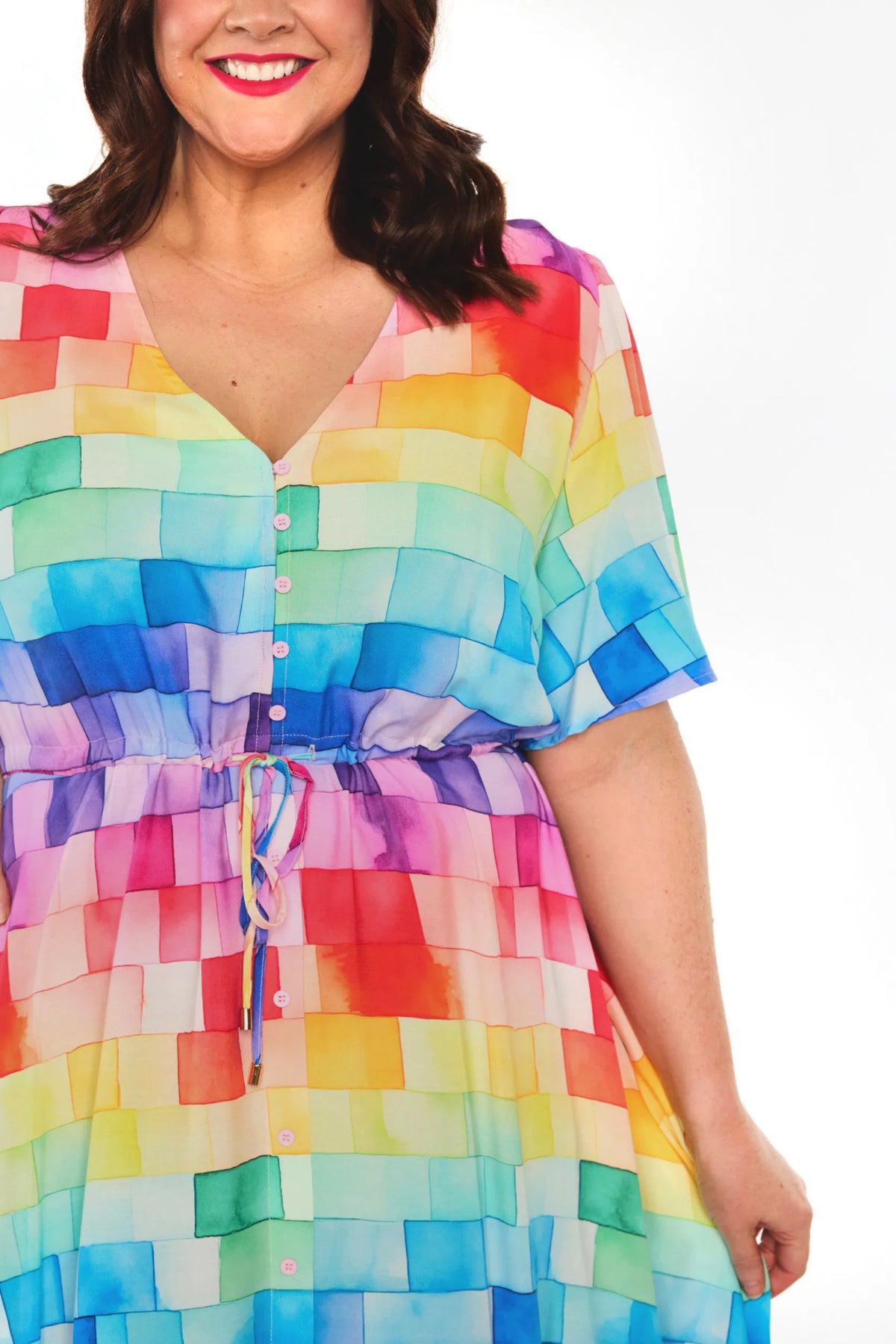 A woman wearing a short-sleeve V-neck dress with a colorful rainbow block pattern and a drawstring waist, shown against a plain white background.