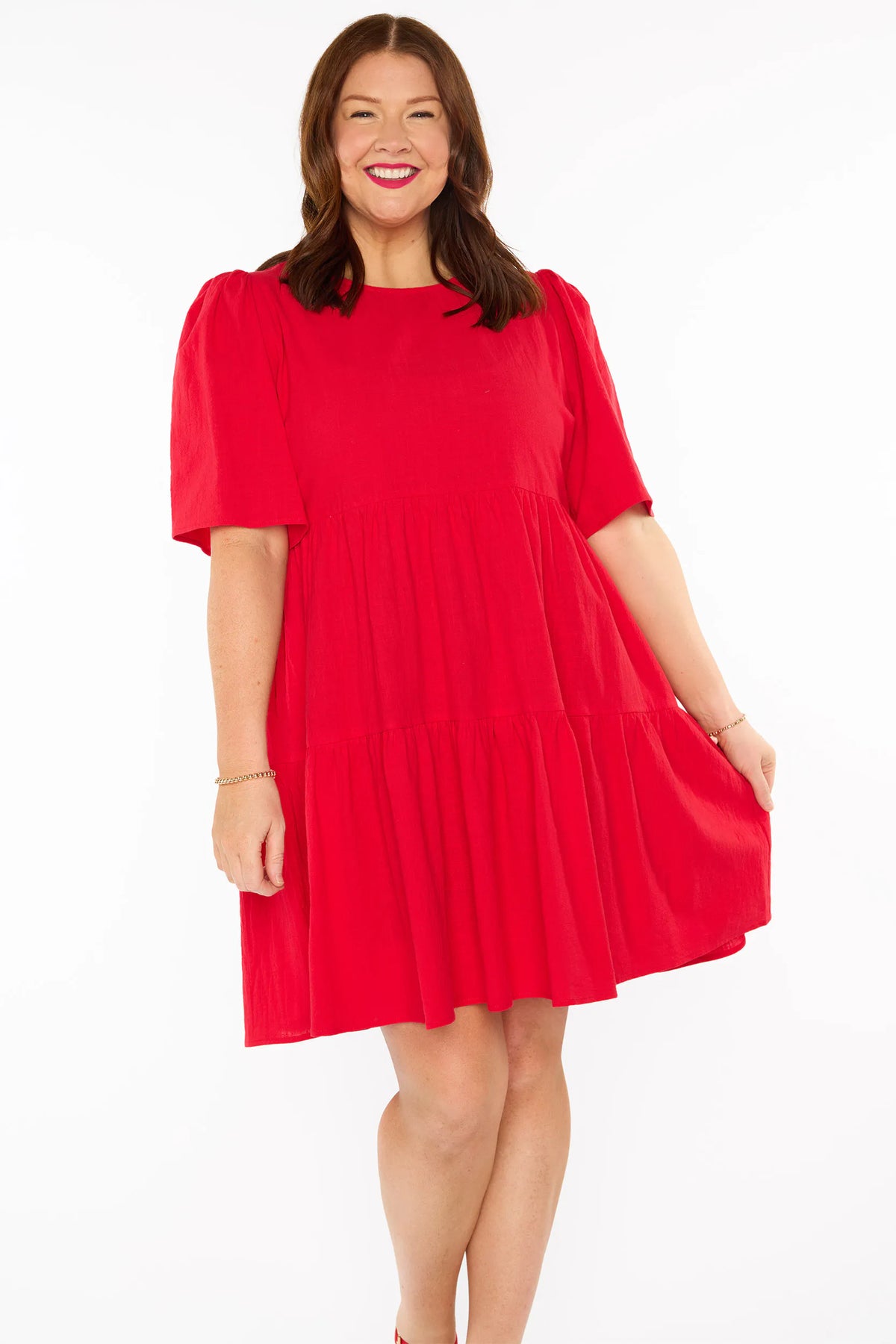 A woman modelling a bright red tiered mini dress with short puff sleeves, against a plain white studio background.