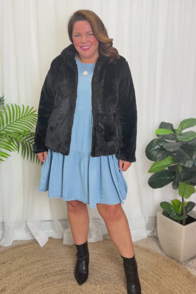Video Woman wearing a black faux fur jacket over a light blue dress on a white background