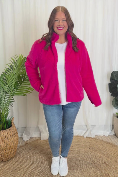 Person wearing a bright pink fleece jacket, white shirt, blue jeans, and white sneakers on a white background